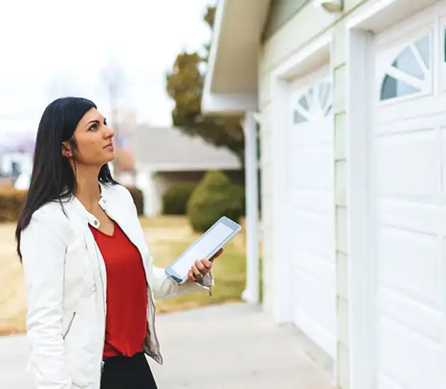 woman wearing a red blouse and white blazer standing outside a home looking at the garage doors